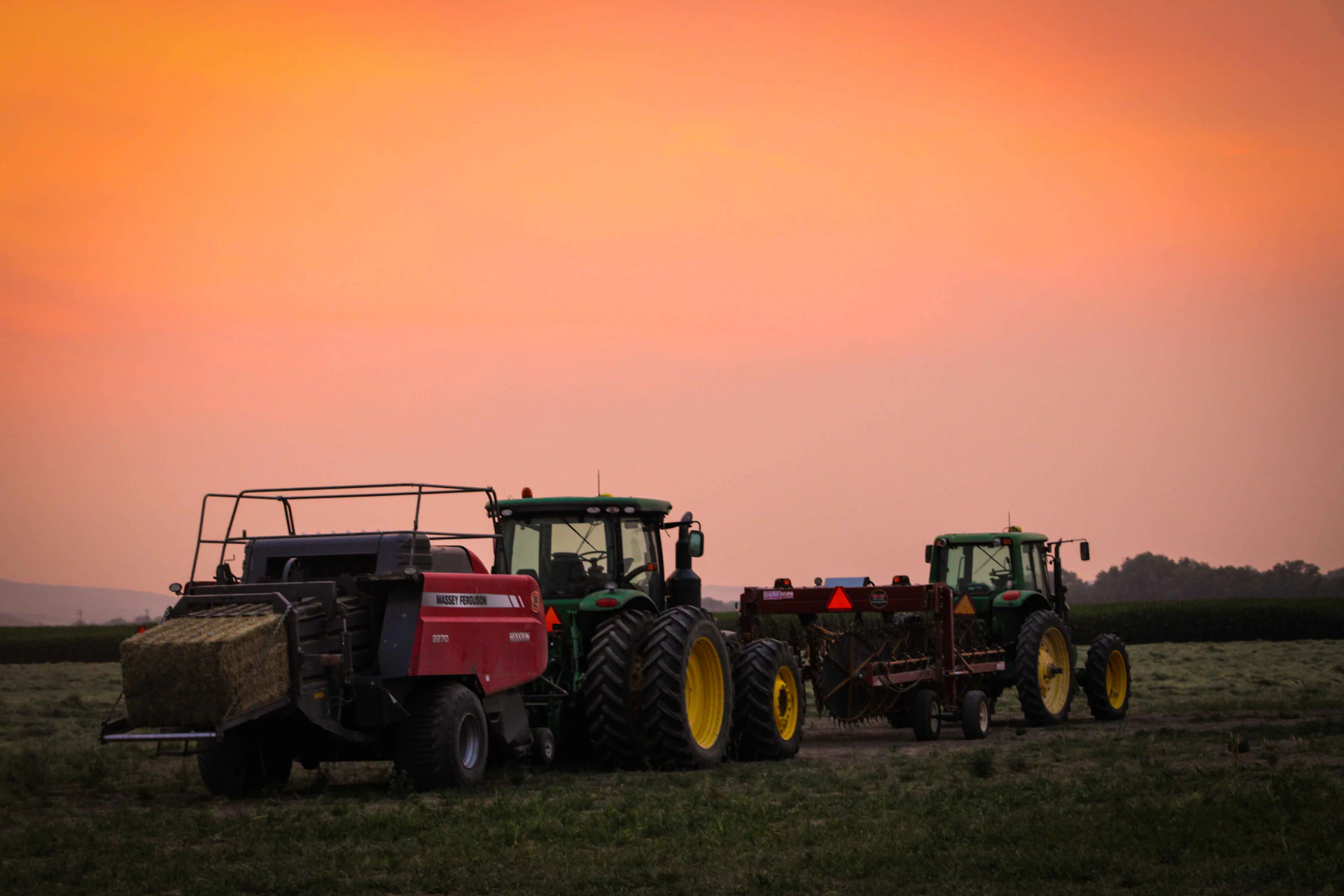 Trattori e rotopressa in un campo al tramonto